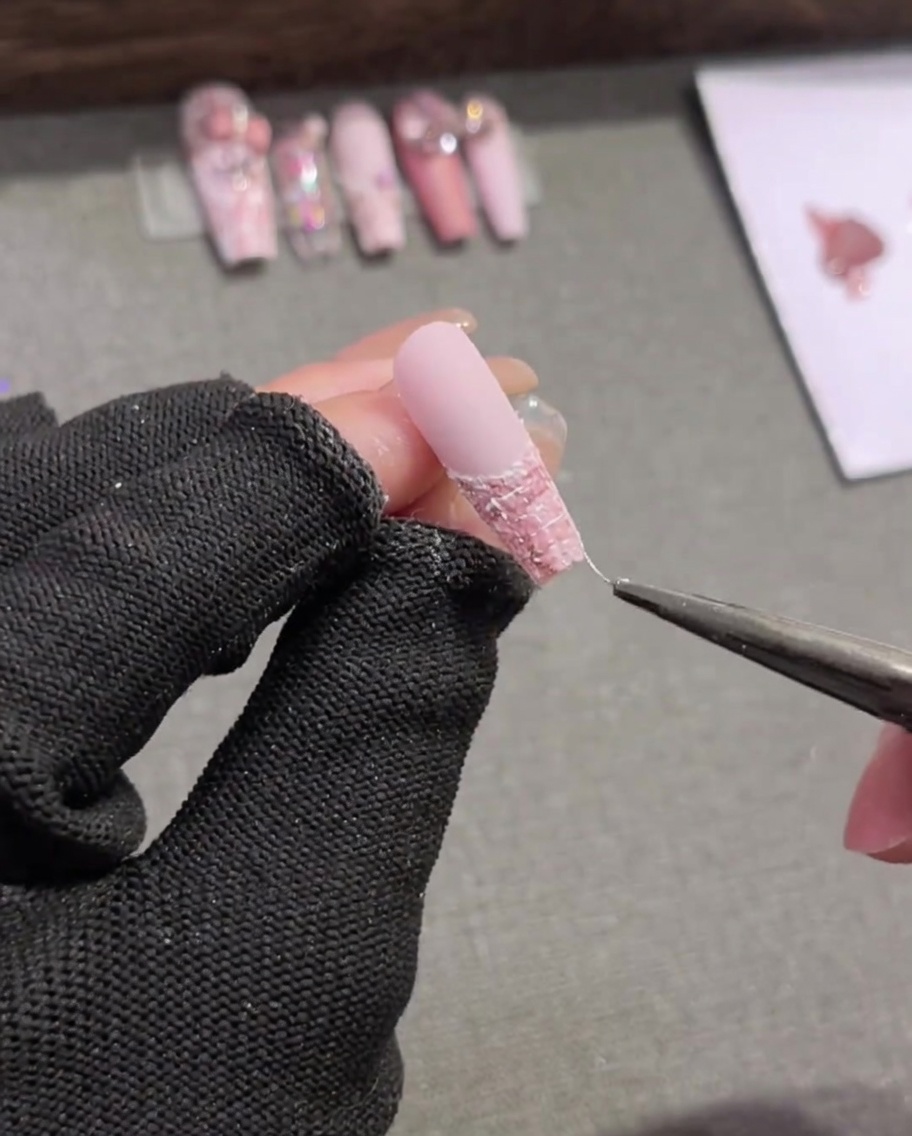 Un pinceau liner dessinant soigneusement de fines lignes horizontales blanches sur un design dongle écossais rose et blanc.