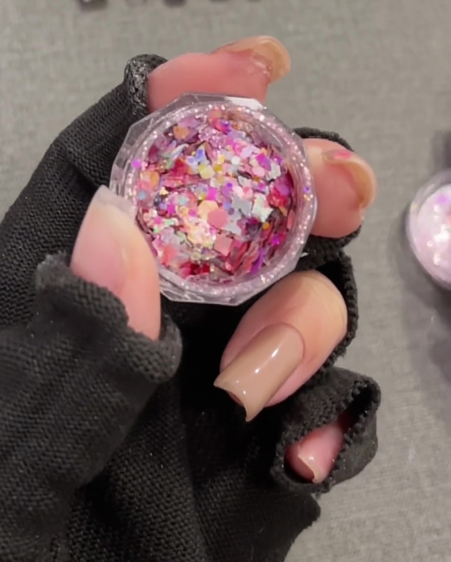 Gros plan dun pinceau plat prélevant des sequins épais, colorés et irisés dun petit pot rond.