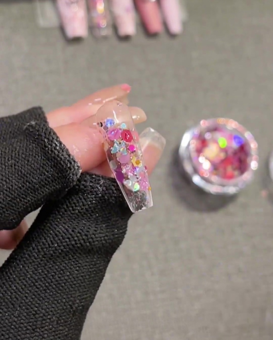Un pinceau appliquant un gel de construction transparent à consistance épaisse sur un ongle décoré de sequins, en le lissant pour créer une surface plane.