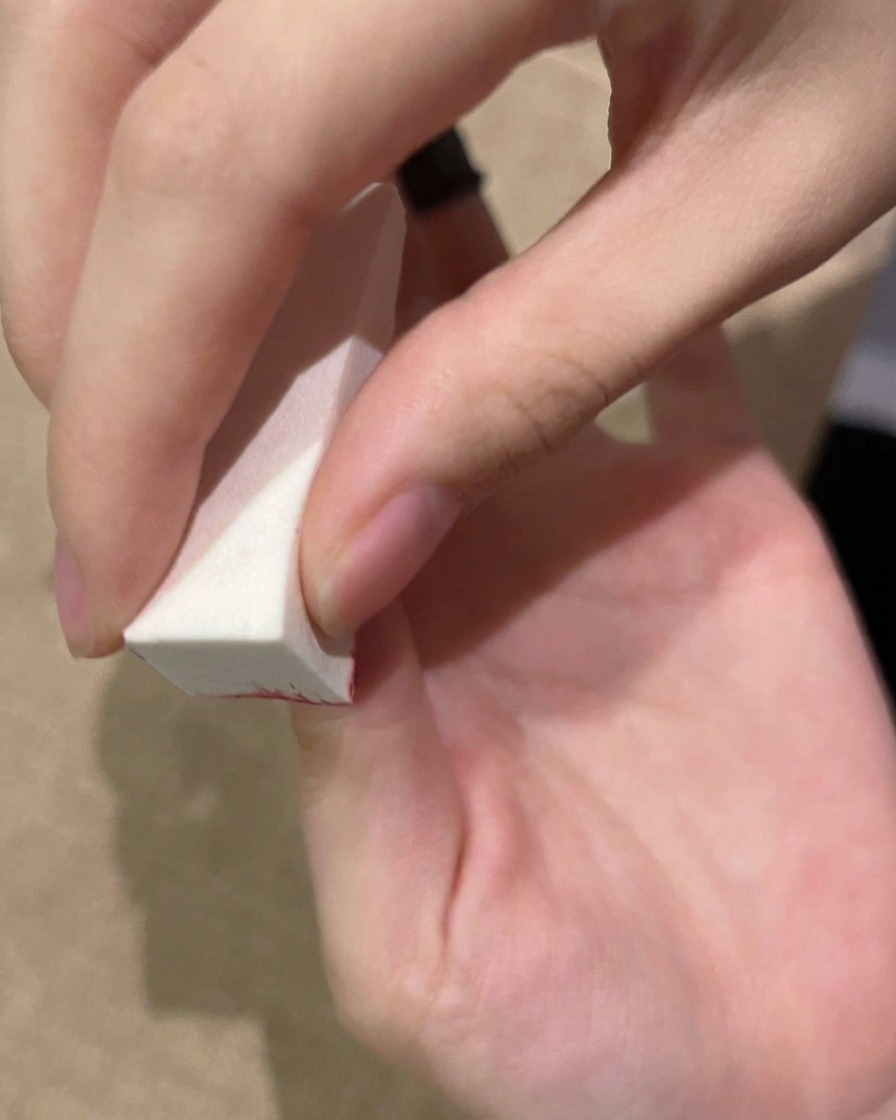 Une main tapotant du gel sur un ongle avec une éponge avant de catalyser sous une lampe UV.