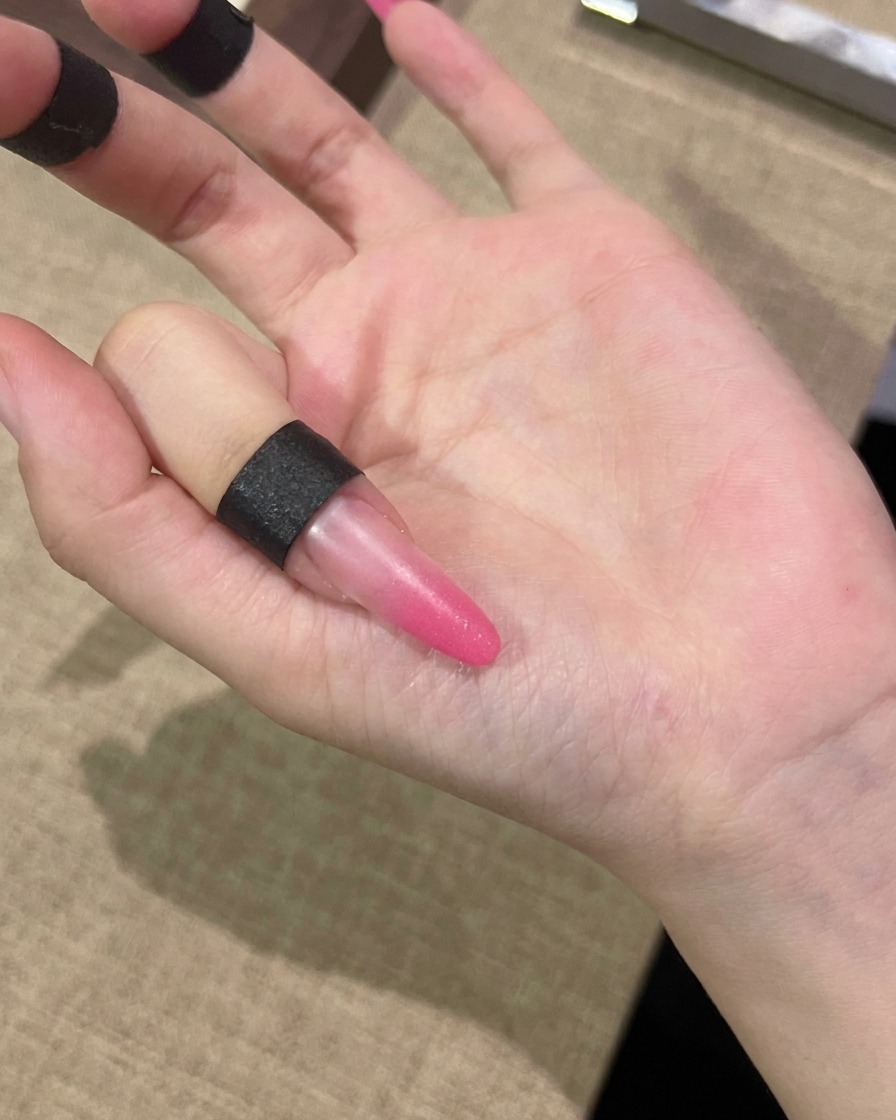 Un pinceau appliquant une couche de gel cat-eye rose sur toute la surface dun ongle.