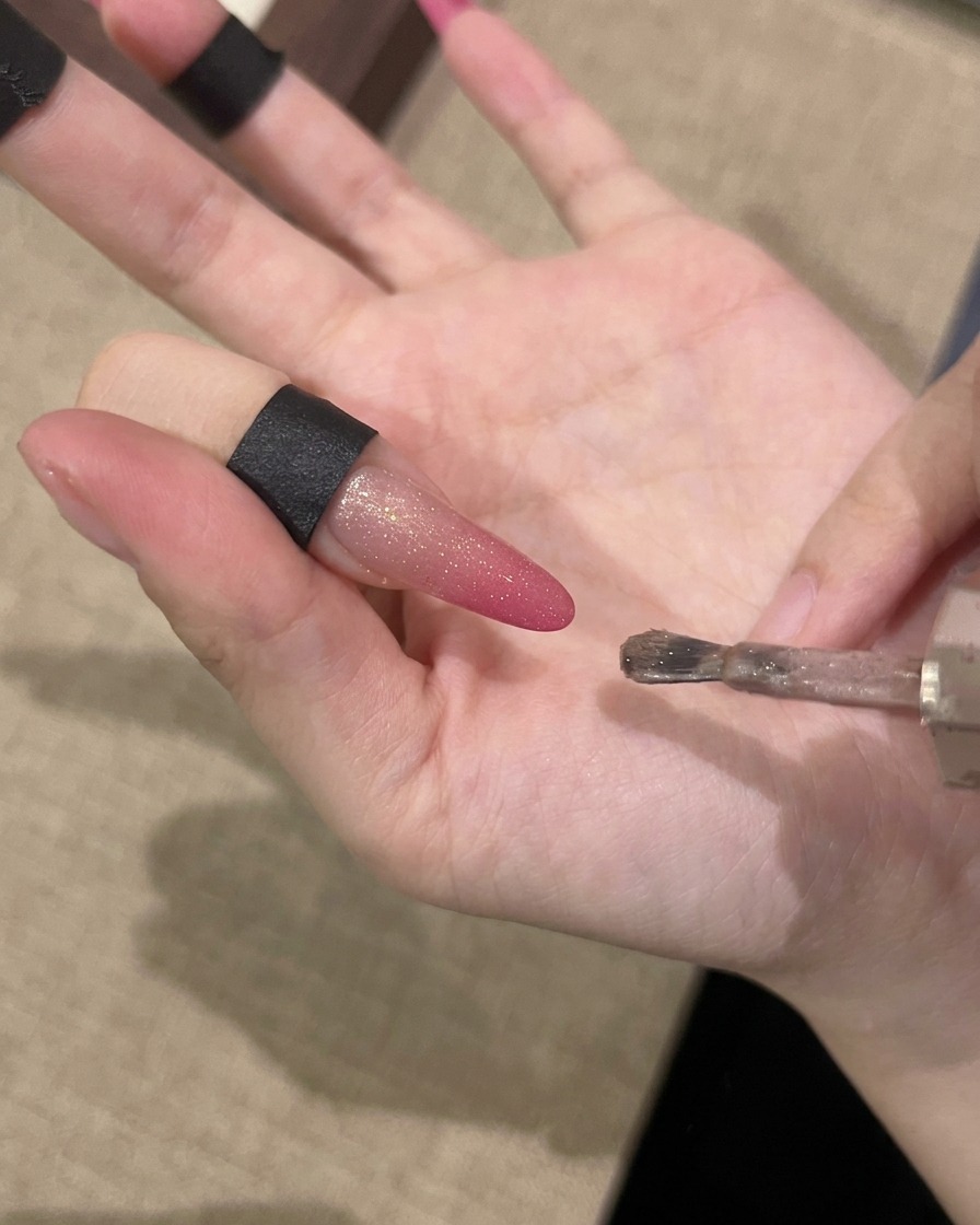 Une main tenant un aimant parallèlement à un ongle pour attirer les particules scintillantes magnétiques.