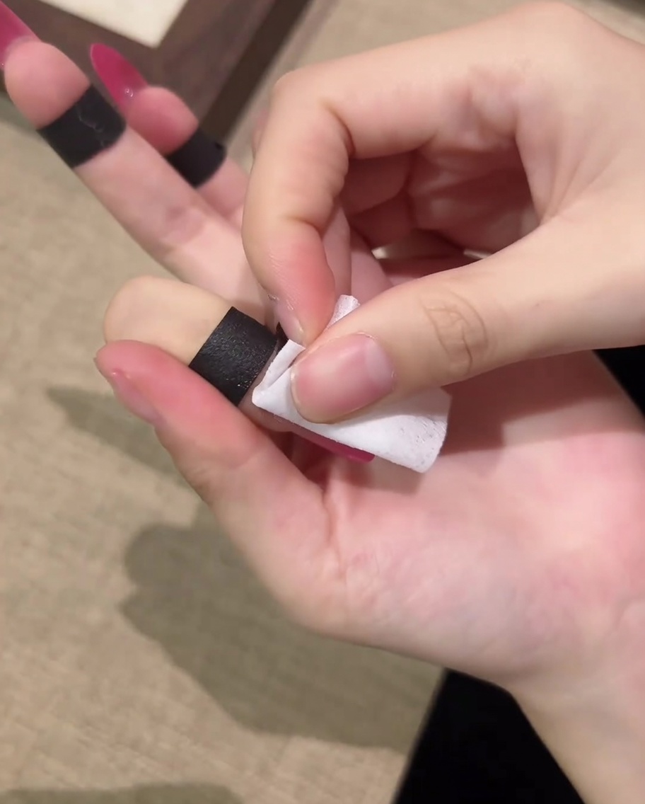 Une main utilisant un coton non pelucheux pour essuyer un ongle catalysé afin déliminer la couche collante.
