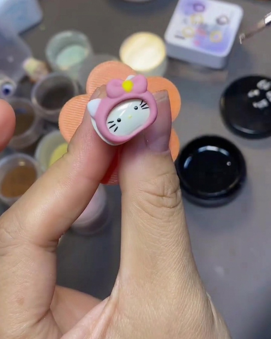 Un pinceau fin de nail art applique un top coat transparent sur une décoration Hello Kitty en 3D.