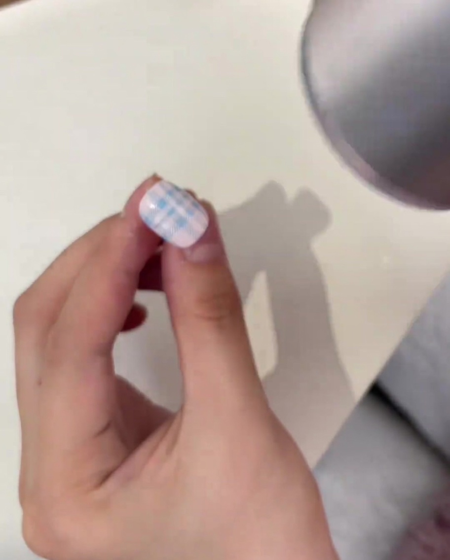 Poudre de cristal transparente saupoudrée sur un motif plaid bleu tamponné sur longle à laide dun pousse-cuticules en métal.