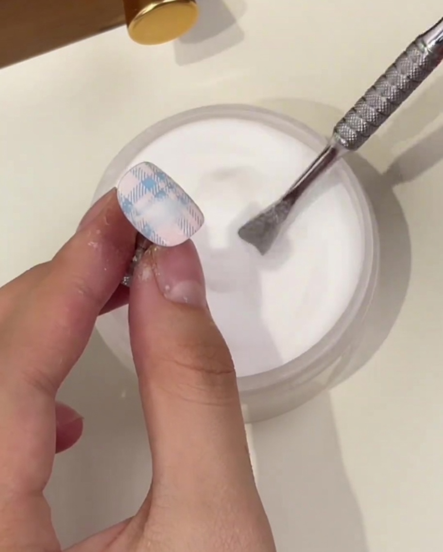 Gros plan sur un ongle avec motif plaid bleu, saupoudré de poudre de cristal au-dessus dun pot.