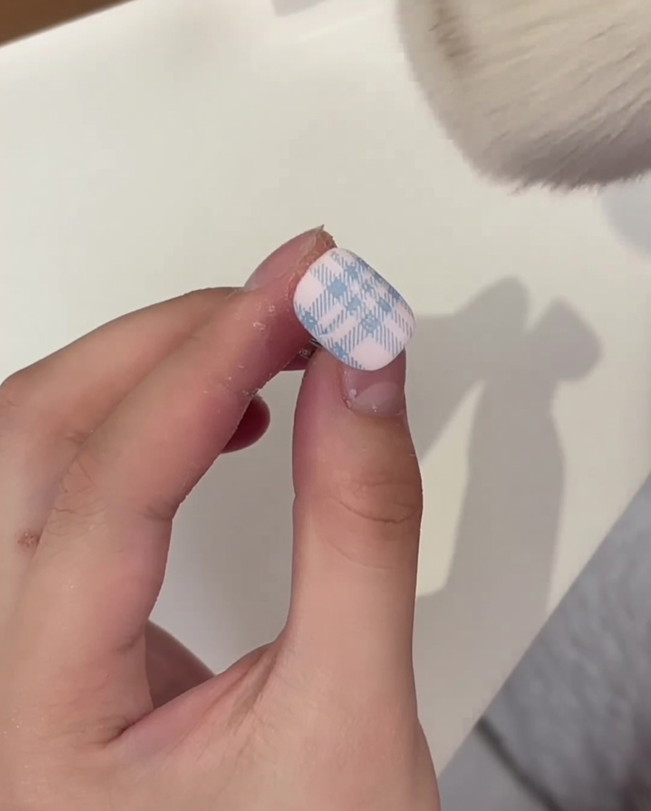 Pinceau de maquillage touffu retirant la poudre de cristal blanche en surplus sur un ongle au motif plaid catalysé.