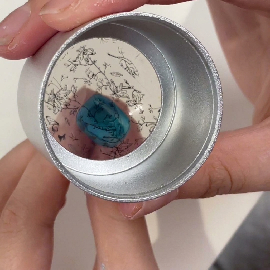 Tampon en gelée tenu au-dessus dun ongle turquoise, montrant le motif floral noir prêt à être transféré.