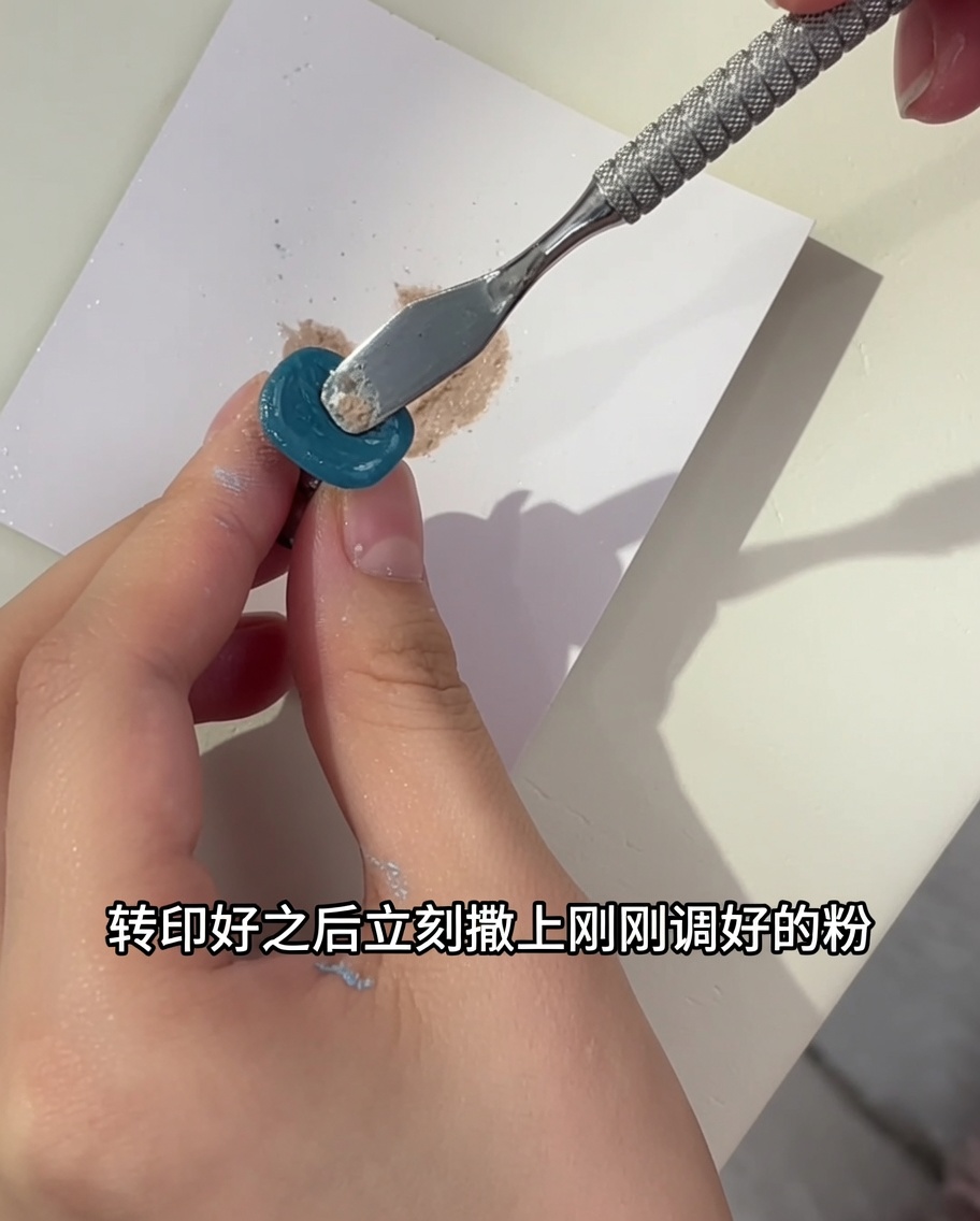 Outil métallique appliquant une seconde couche de mélange de poudre scintillante sur un ongle floral.