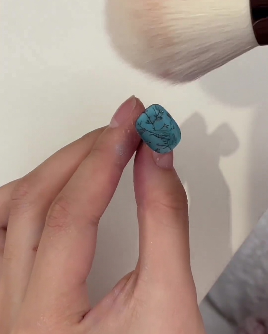 Pinceau type maquillage retirant la poudre en surplus sur un ongle turquoise après catalysation.