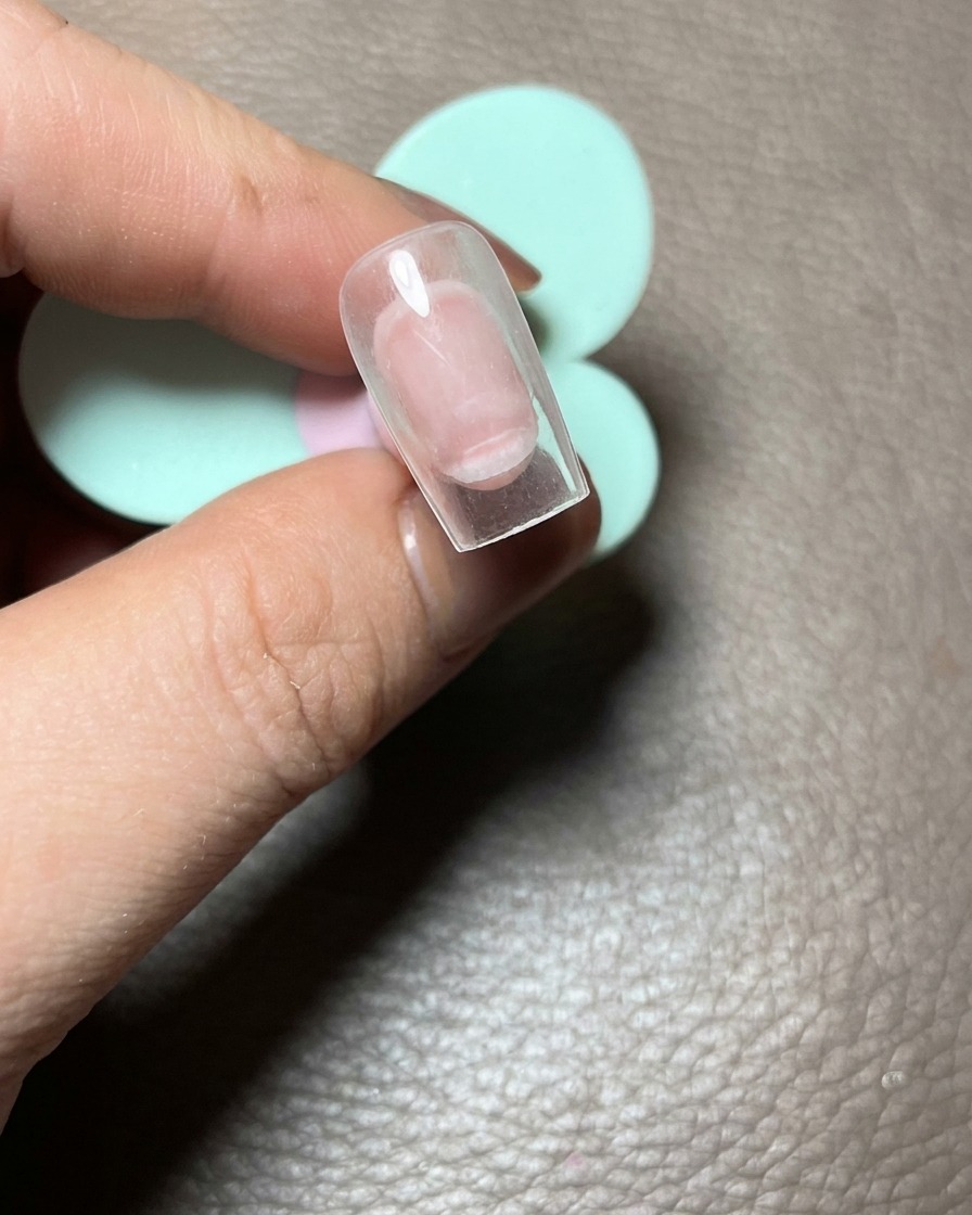 Vue rapprochée dun ongle sur capsule transparente tenu par une main, montrant trois points de gel rose formant la base de la patte.
