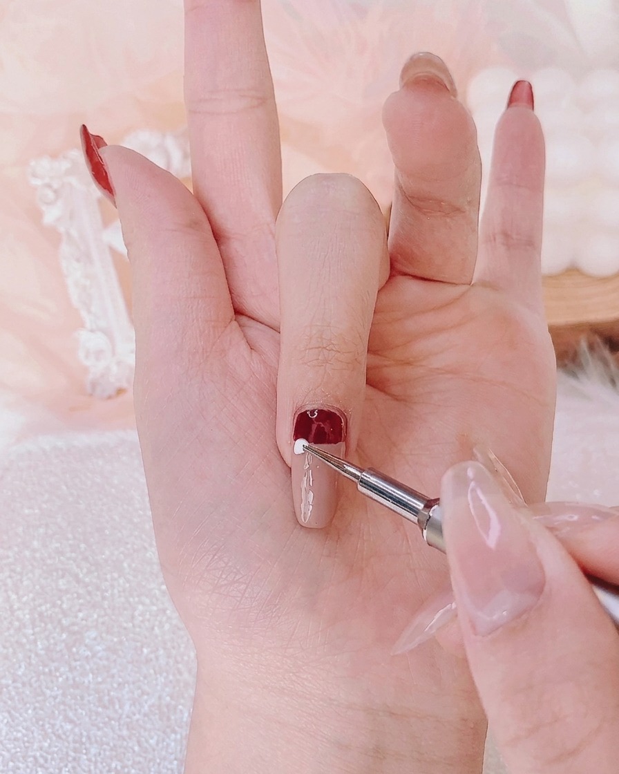Un outil de dotting appliquant un point précis de gel blanc au centre dun ongle pour former un élément du design.