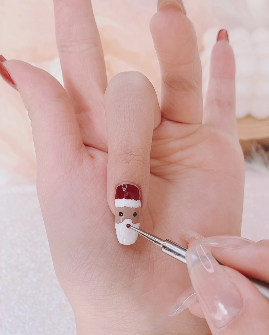 Un pinceau liner fin ajoutant deux minuscules points noirs sur un ongle pour représenter les yeux dun personnage.