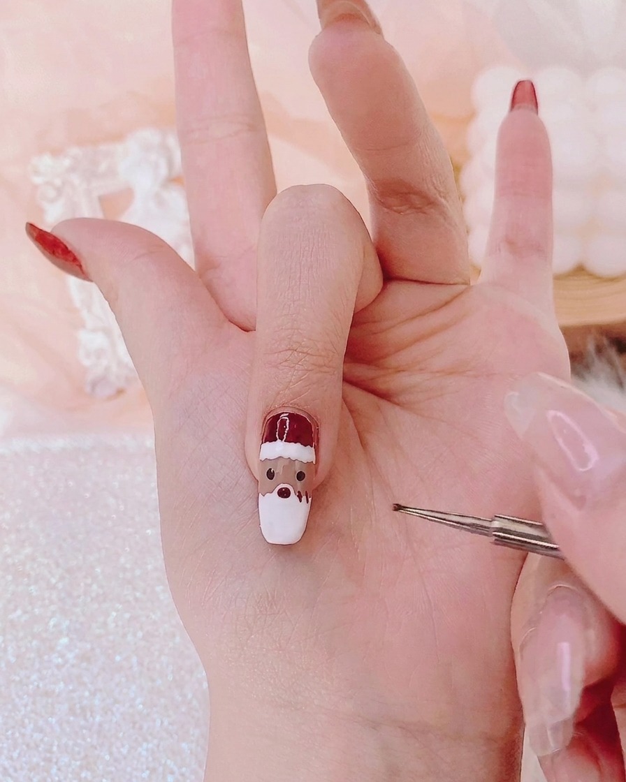 Un pinceau de détail fin appliquant des points de gel rouge au centre du visage dun personnage sur un ongle.
