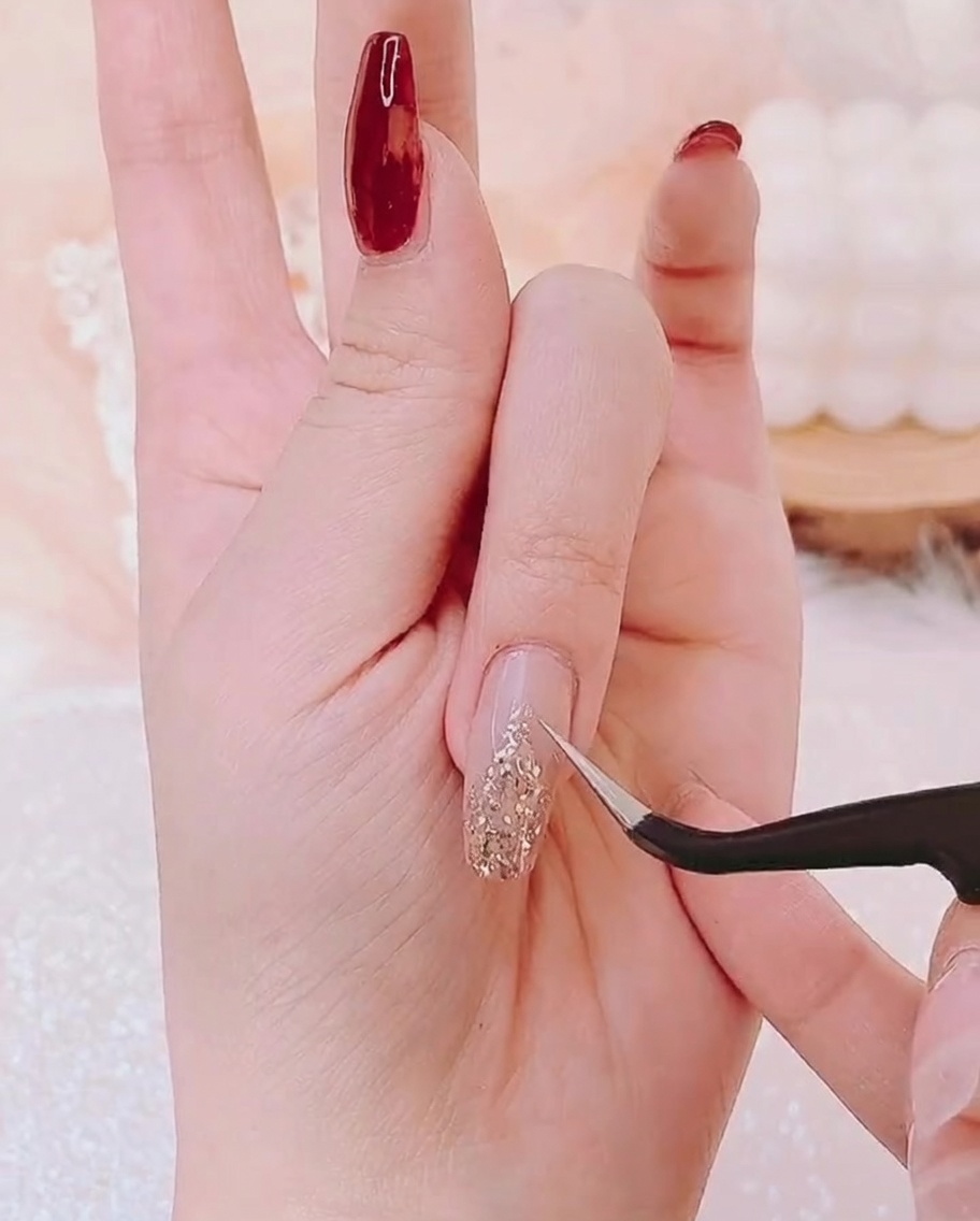 Une pince à épiler plaçant un petit charm étoile dorée à la pointe de la base en paillettes dorées.