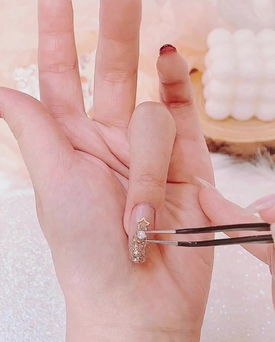 Une pince positionnant une minuscule perle sous létoile dorée parmi dautres petits strass.