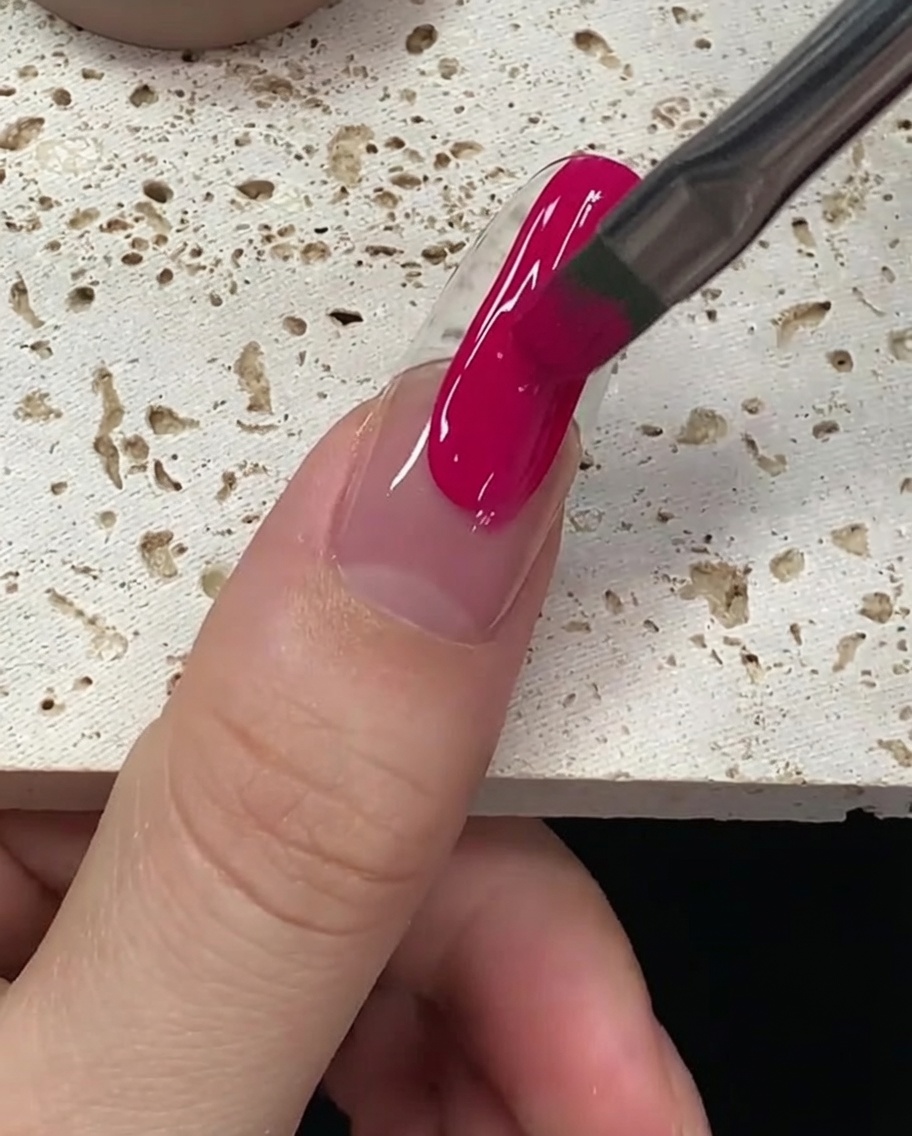 Le pinceau égalisant le vernis gel magenta pour assurer une couverture totale et uniforme.