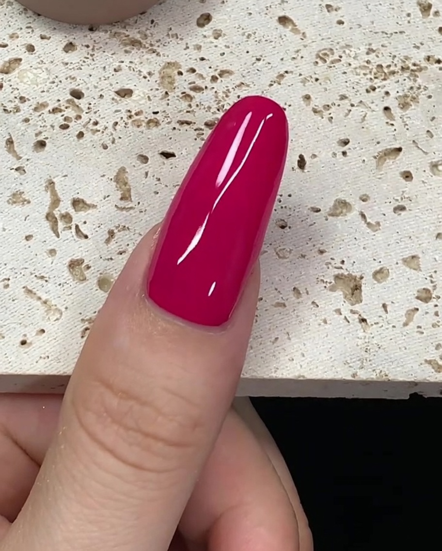 Un pinceau chargé de vernis gel rouge profond près de la cuticule dun ongle.