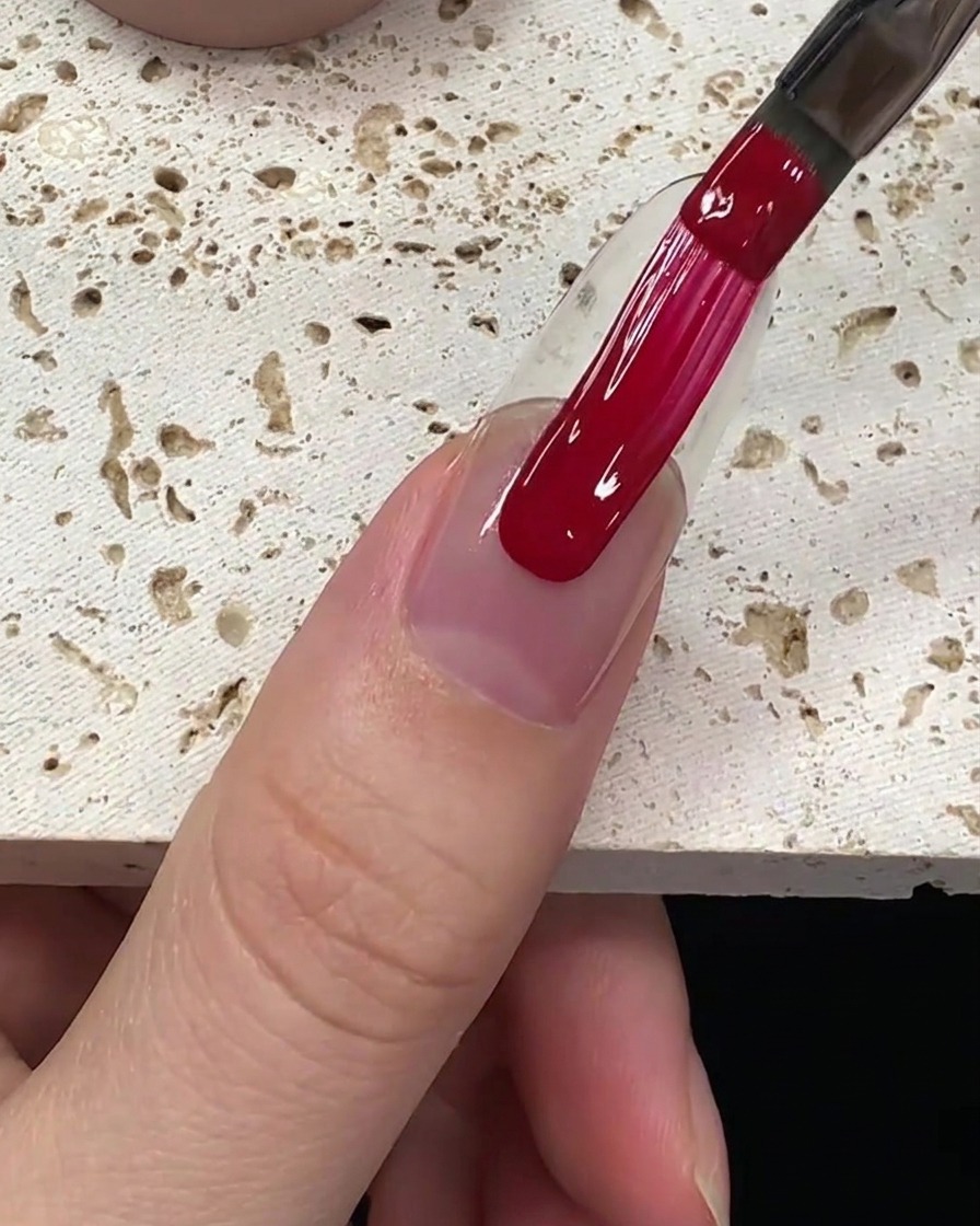 Application lisse du vernis gel rouge profond sur la plaque de longle.