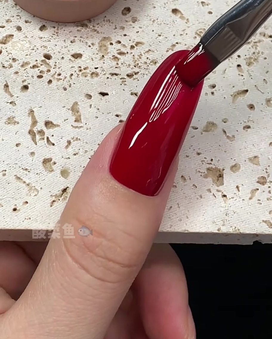 Gros plan sur un pinceau perfectionnant les bords dun ongle recouvert de vernis rouge.
