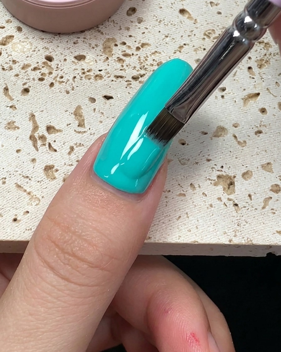 Gros plan montrant les derniers traits de vernis vert menthe lissés jusquà lextrémité de longle.