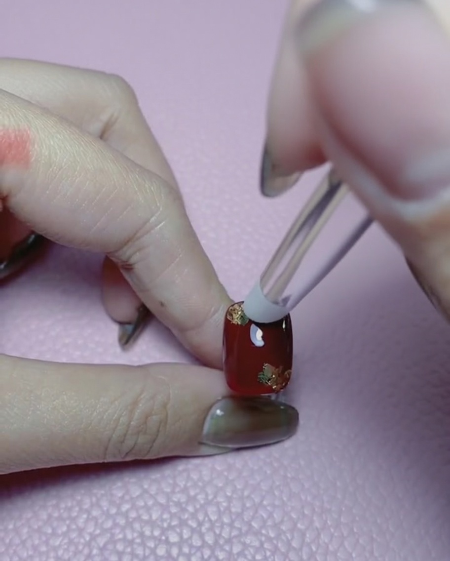 Gros plan dun outil en silicone lissant la feuille dor sur un ongle rouge.