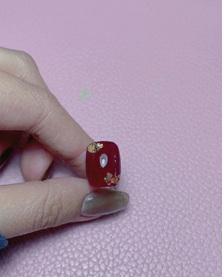 Gros plan dun ongle rouge avec des accents de feuilles dor, recouvert dun top coat brillant.