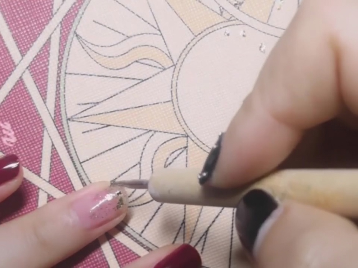 Un stylet de nail art plaçant un délicat flocon de feuille dor au centre dun ongle recouvert de base coat collante.