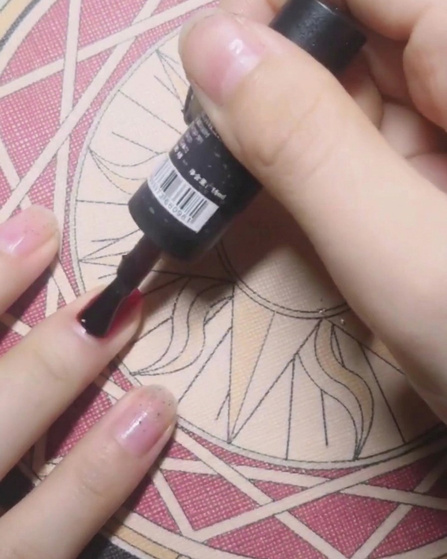 Un pinceau de flacon appliquant du base coat sur un ongle en préparation du vernis gel rouge.