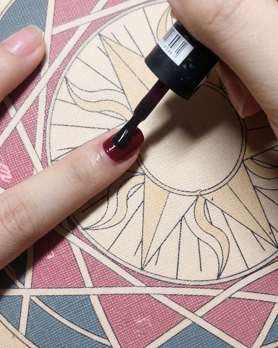 Un pinceau appliquant un vernis gel bordeaux profond sur un ongle, créant une couleur opaque et solide.