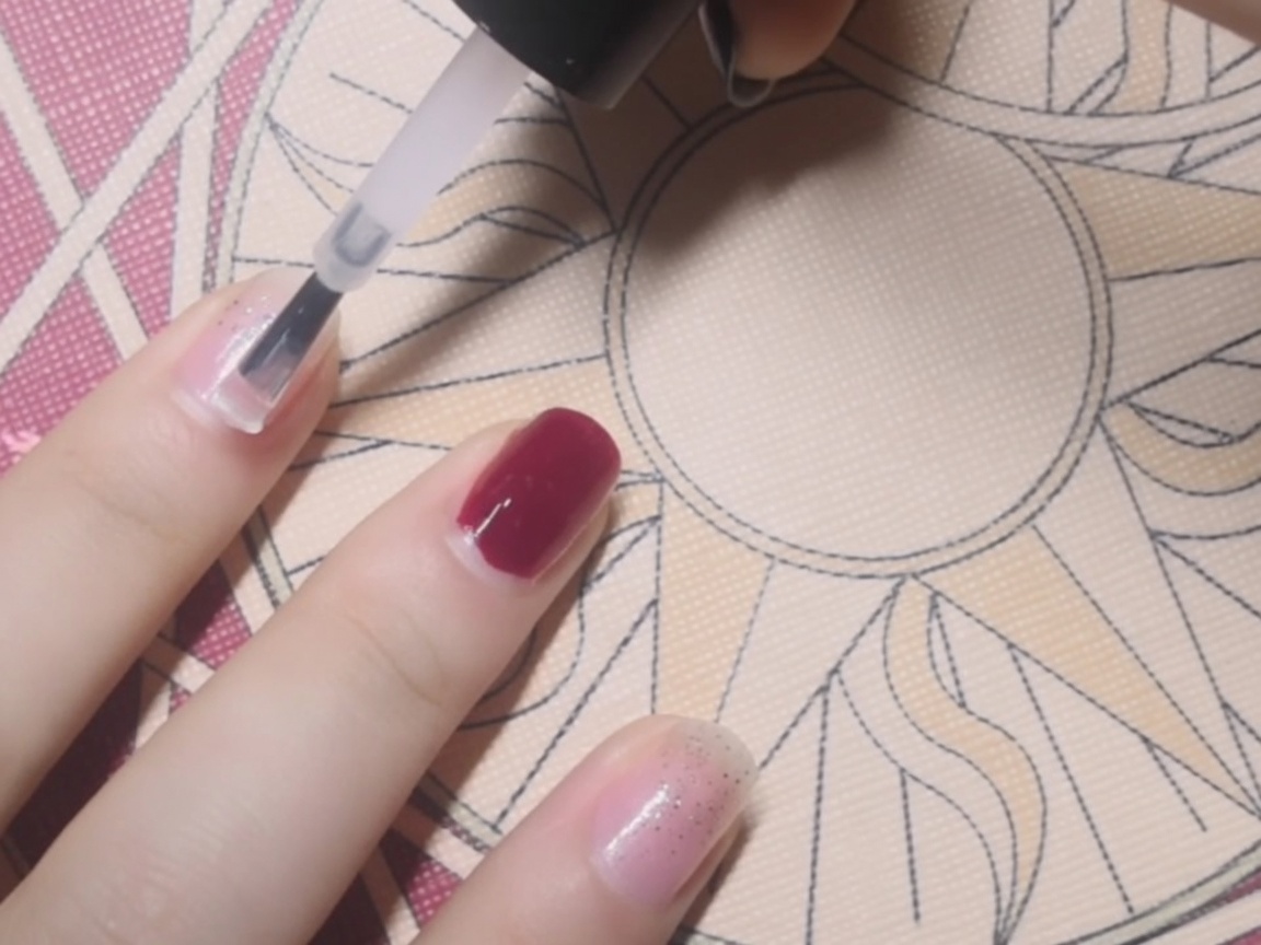 Gros plan dune base coat transparente appliquée au pinceau sur un ongle.