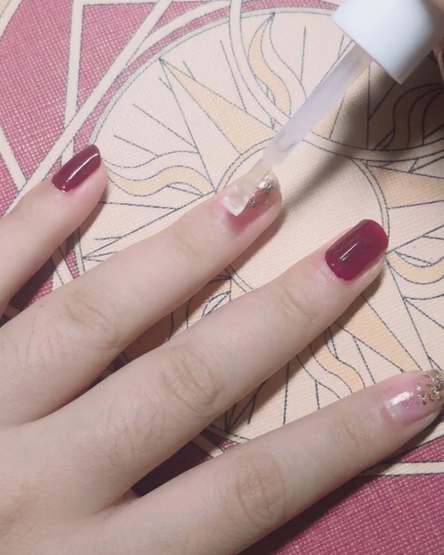 Un pinceau appliquant un top coat transparent sur un ongle décoré de feuilles dor.