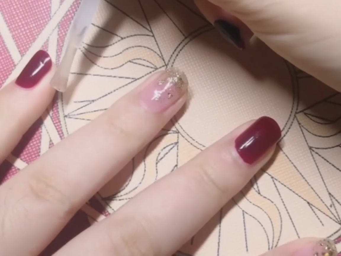Application dun top coat transparent sur un ongle rouge uni.
