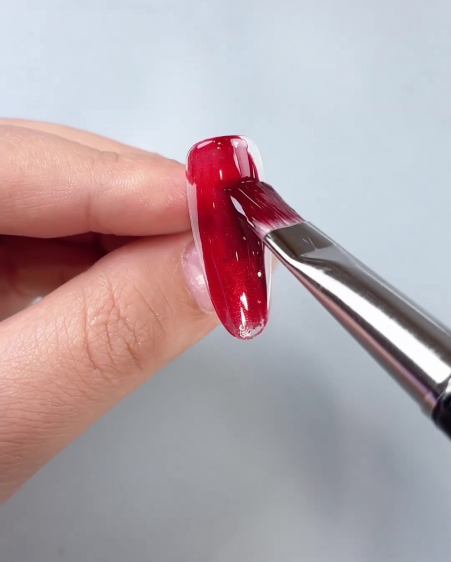 Un pinceau appliquant du gel œil de chat rouge au centre dune capsule dongle transparente.