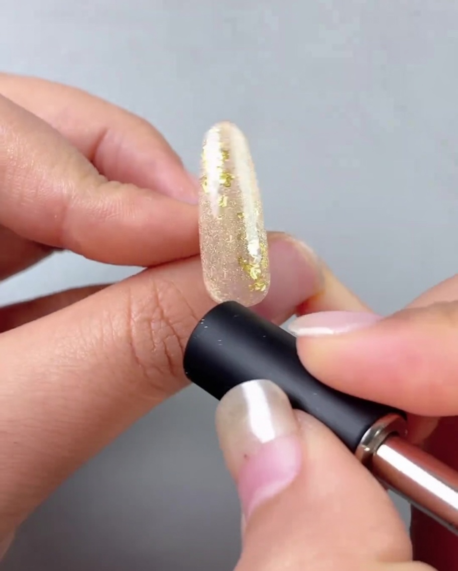 Un aimant à ongles tenu près dun ongle peint avec du gel doré pour créer une ligne réfléchissante œil de chat.