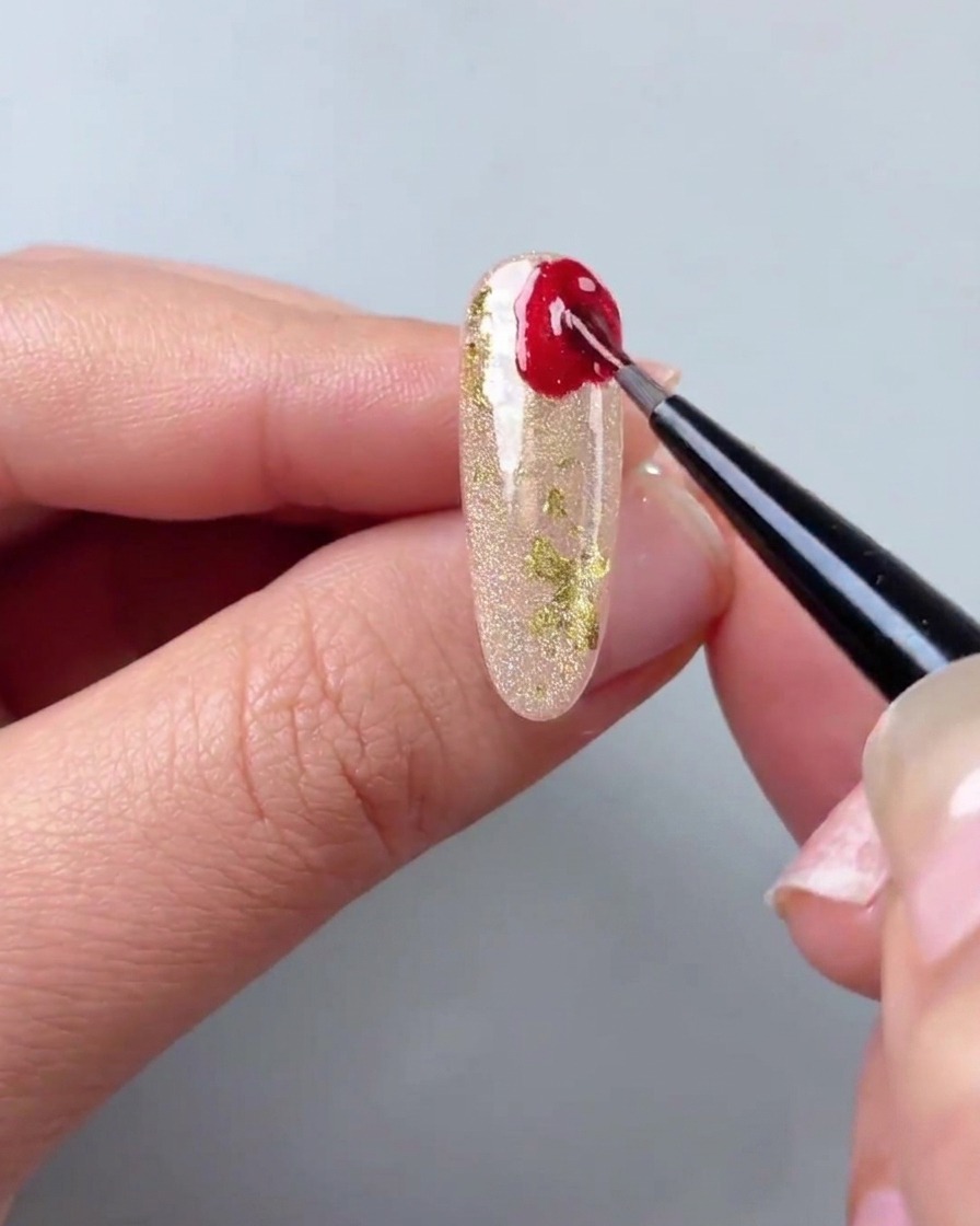 Un pinceau fin de détail appliquant du gel œil de chat rouge aux formes irrégulières dans le coin dun ongle doré scintillant.