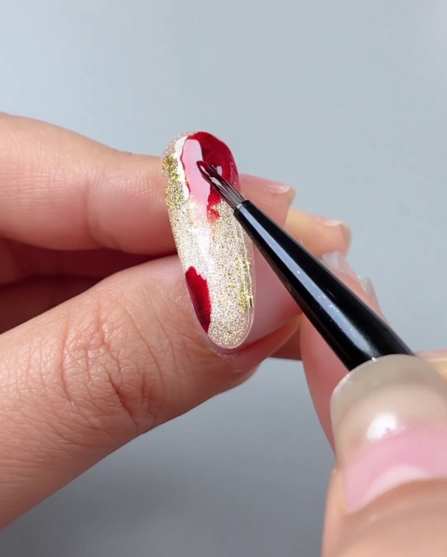 Un pinceau à ongles fondant des taches de gel rouge en un dégradé en utilisant du gel aquarelle.