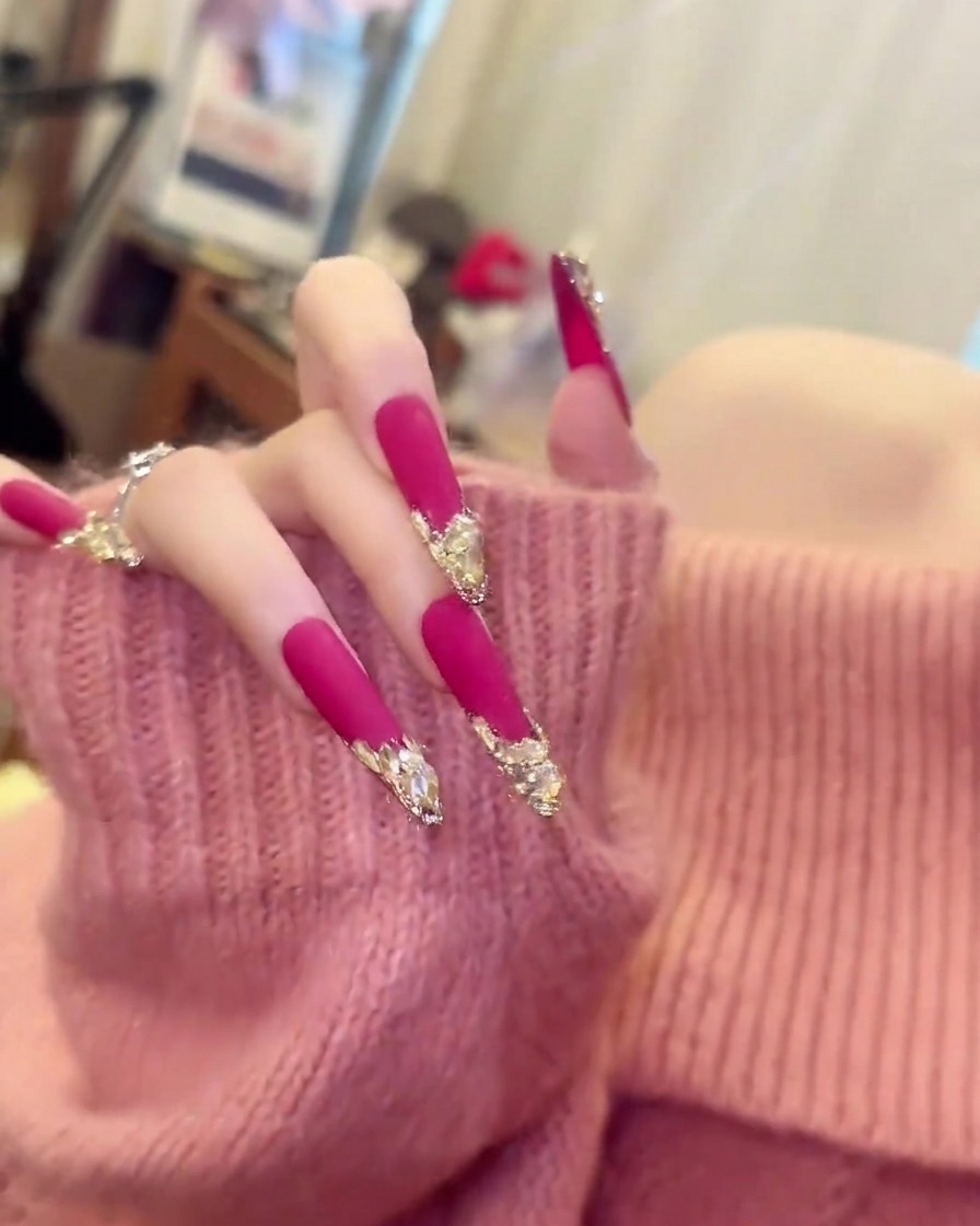 Une main avec un pull rose pâle bougeant doucement pour montrer la longueur et la courbure des longs ongles amande rose mat.