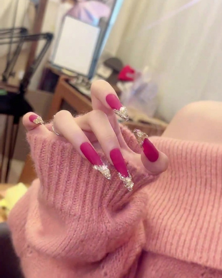 Gros plan net sur un doigt montrant le placement précis des clusters de cristaux sur le vernis rose vif mat.