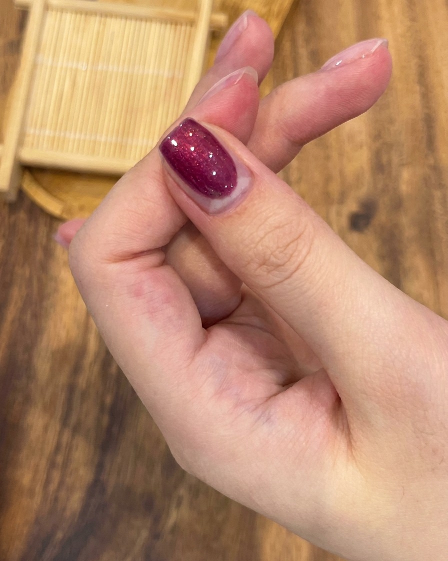 Un pinceau professionnel appliquant uniformément un vernis gel magnétique rose rouge sur un ongle.