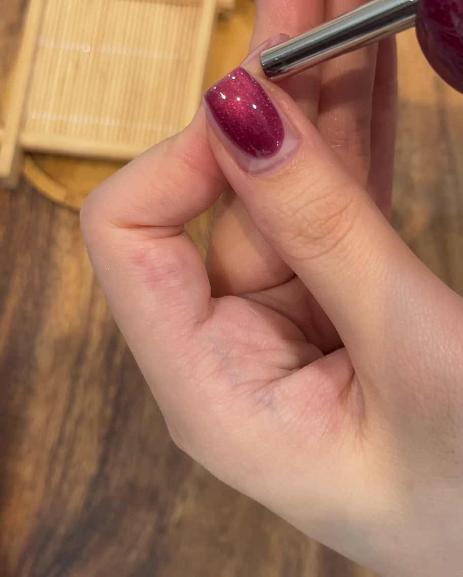 Gros plan dun aimant rectangulaire maintenu au-dessus dun ongle verni pour former une ligne de reflets.
