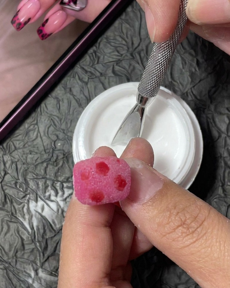 Gros plan sur un pinceau liner traçant de petites taches noires irrégulières sur un ongle rose texturé.