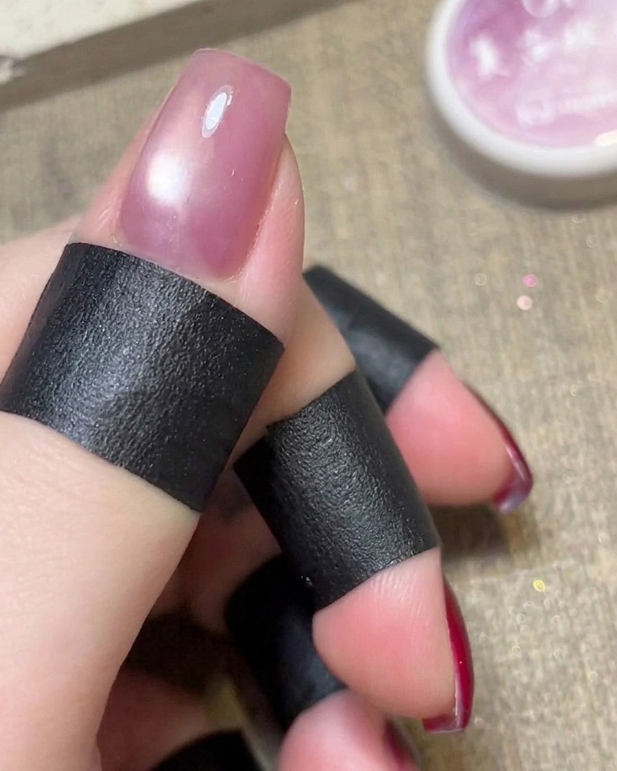 Un aimant cylindrique maintenu au-dessus dun vernis rose cat-eye humide sur un ongle.
