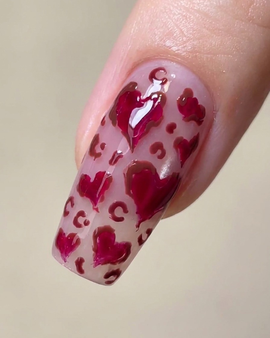 Gros plan dun ongle avec des cœurs magenta et de délicates taches léopard marron entre eux.