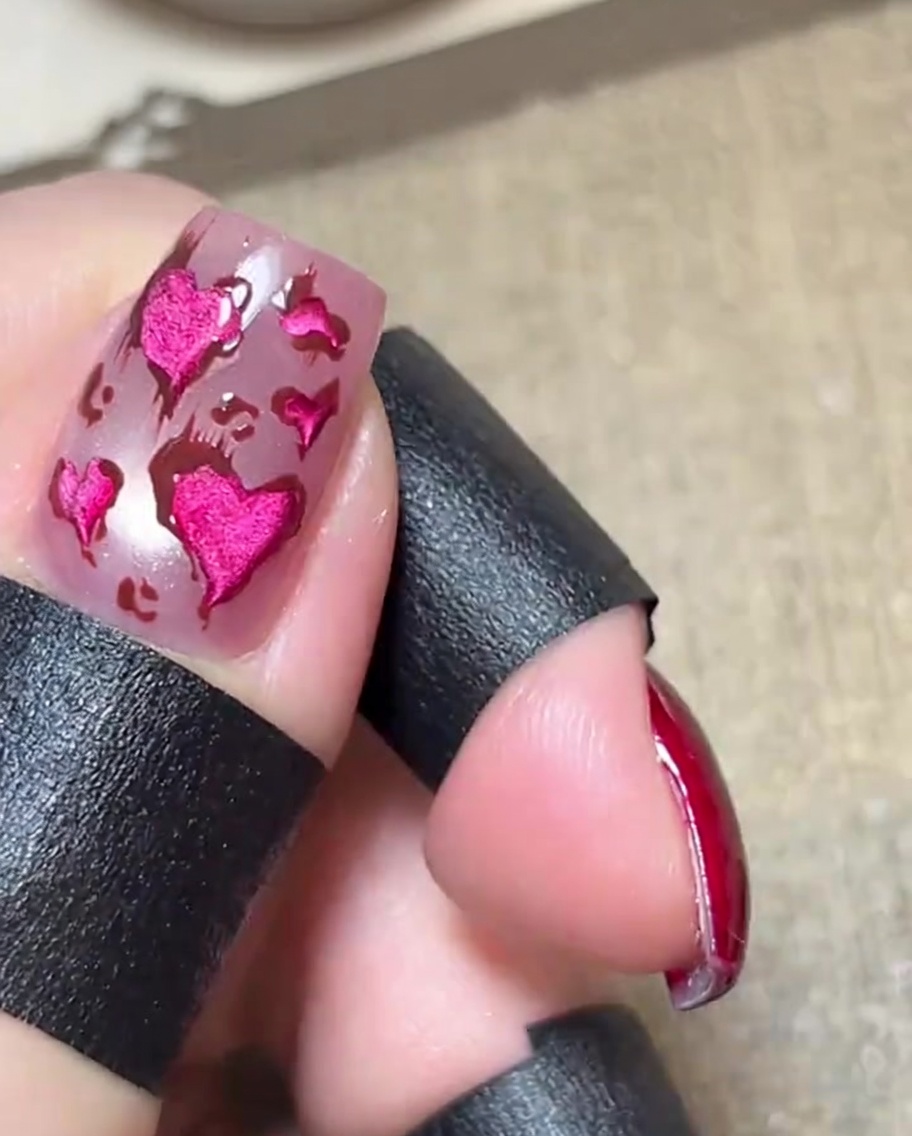 Gros plan dun ongle rose brillant avec des cœurs rose métallique contourés de marron, et de fines lignes délicates.