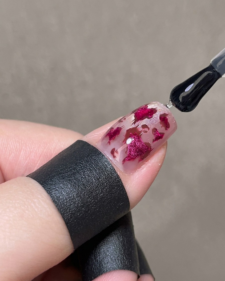 Un pinceau appliquant une couche épaisse de gel brillant transparent sur un ongle décoré.