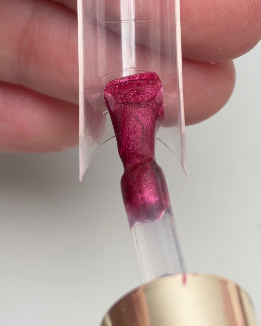 Un pinceau appliquant du vernis gel magenta sur une forme dextension dongle transparente.