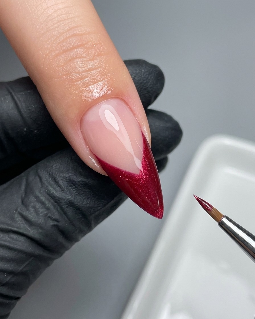 Un pinceau liner fin perfectionnant soigneusement le bord dune French magenta sur un ongle.