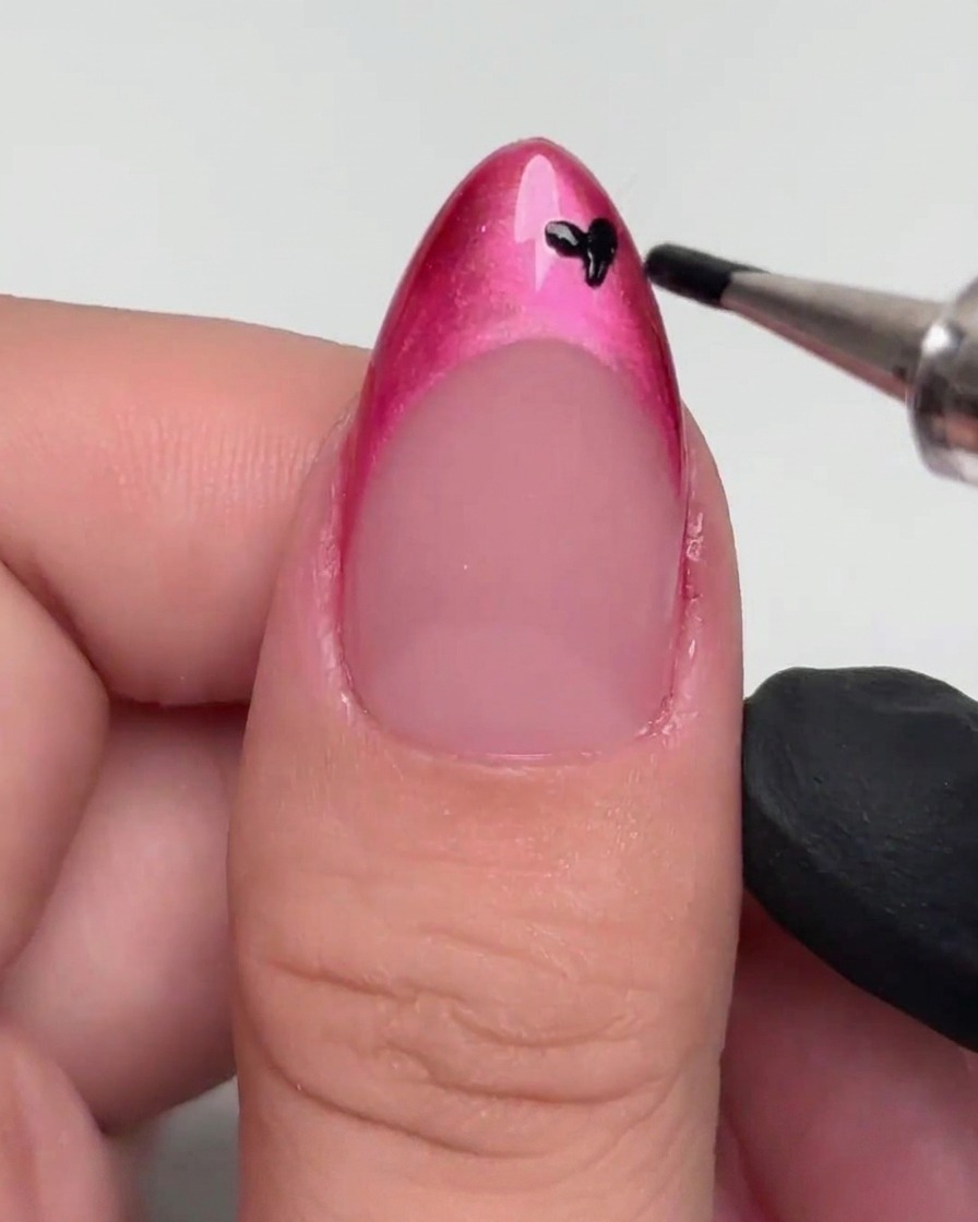 Un outil de pointage appliquant de petites taches noires sur une French manucure peinte en magenta.