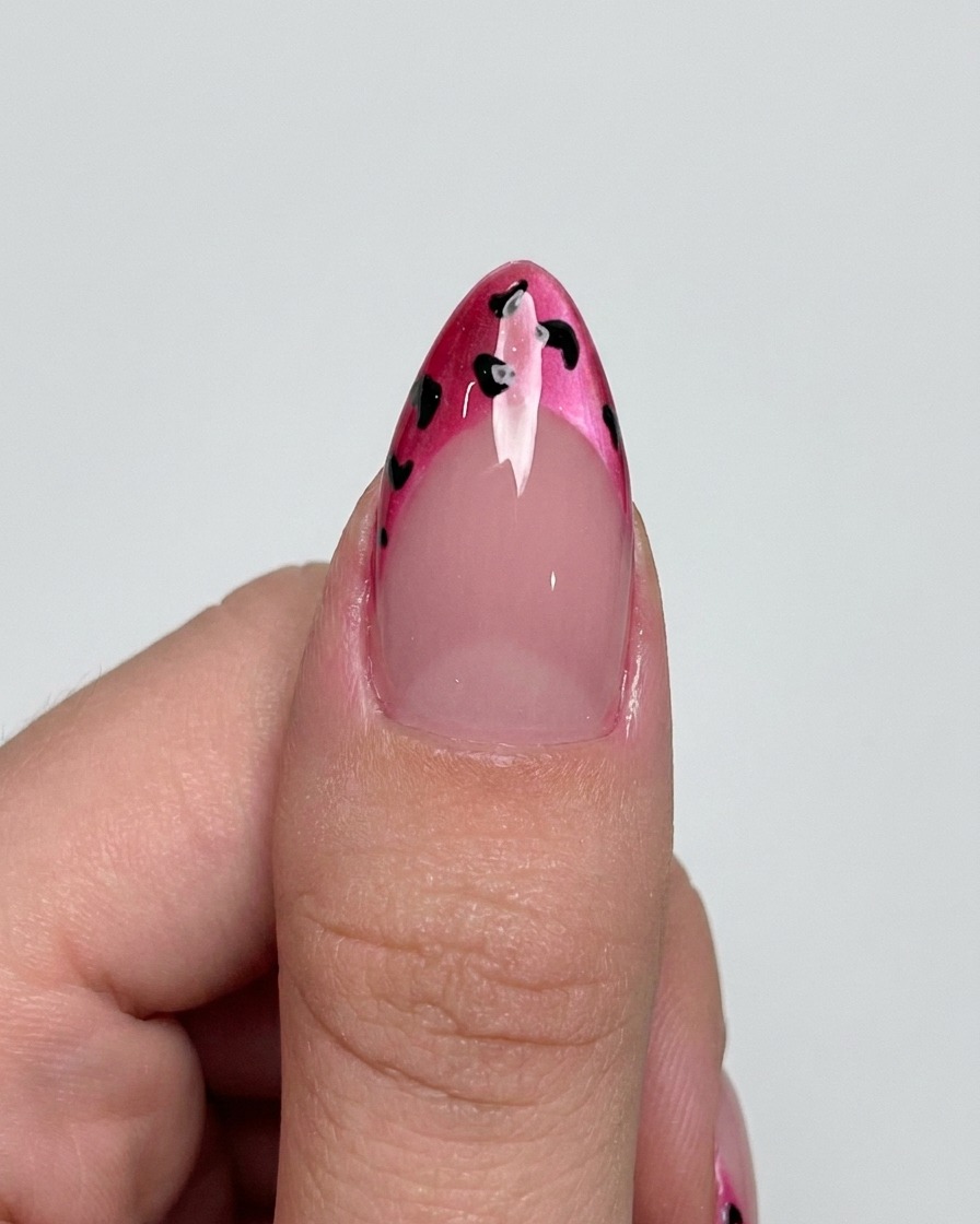 Un pinceau liner ajoutant des contours noirs délicats autour des points sur une French magenta.